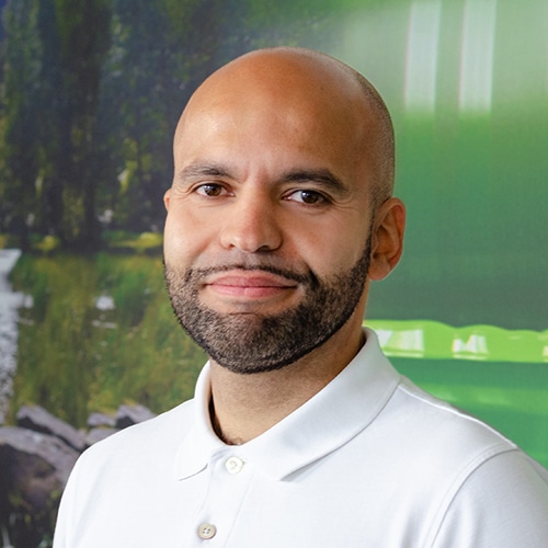 Porträt von Ernesto Bauer, einem Mann mit Glatze und Bart, der ein weißes Poloshirt trägt und leicht lächelt. Er ist Leitung Vertriebsinnendienst / Head of Customer Service bei Debatin.