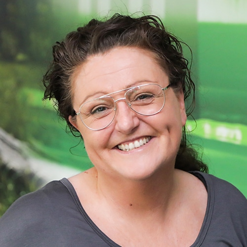 Dieses Bild zeigt Nicole Klingler, die Technische Vertriebsmitarbeiterin bei Debatin. Sie ist auf einer Nahaufnahme lächelnd mit lockigem Haar, Brille und einem grauen Oberteil zu sehen.