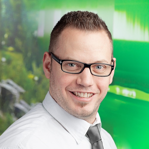 Porträt von Florian Klonig, dem engagierten Leiter des Versand / Shipping Department bei Debatin. Sein breites Lächeln und die markante Brille prägen sein Gesicht, umrahmt von kurzen, dunklen Haaren und einem gepflegten Kinnbart.