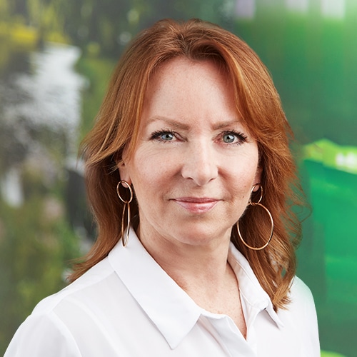 Porträt von Francoise Mathieu, einer engagierten Mitarbeiterin im Vertriebsinnendienst bei Debatin. Sie blickt mit einem sanften Lächeln in die Kamera und hat rotbraunes Haar sowie auffällige, goldene Creolen.