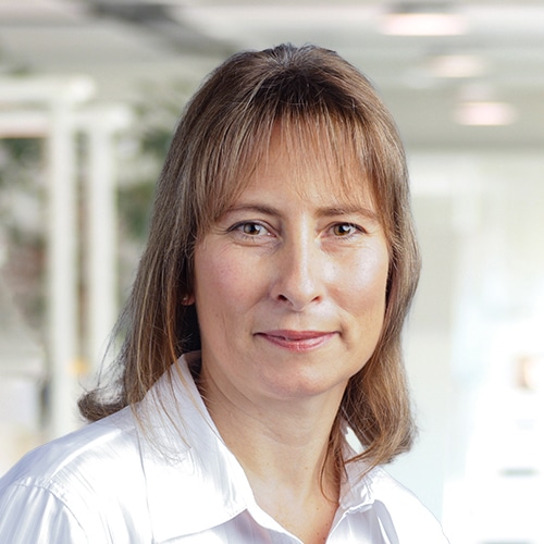 Detailansicht von Sandra Däschner, einer Mitarbeiterin im Einkauf / Purchasing Department bei Debatin. Sie präsentiert sich mit einem offenen, freundlichen Ausdruck und trägt eine klassische weiße Bluse. Ihr schulterlanges, brünettes Haar umrahmt ihr Gesicht vor einem sanft verschwommenen, hellen Hintergrund.