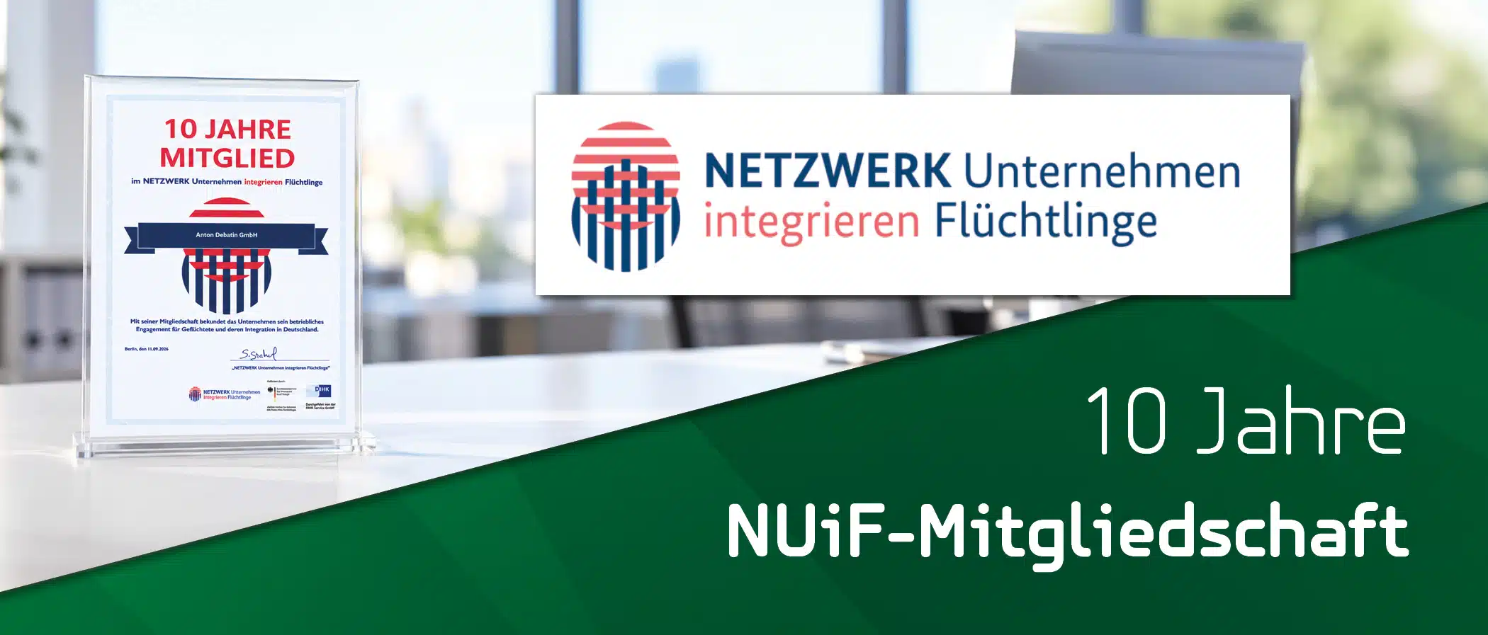 260002ADB_Blogheader_KW40_Auszeichnung_ Unternehmen integrieren Flüchtlinge_2100x897px_Lay01_DE Eine Urkunde zur zehnjährigen Mitgliedschaft der Anton Debatin GmbH im NETZWERK Unternehmen integrieren Flüchtlinge steht in einem transparenten Aufsteller auf einem Schreibtisch. Rechts sind das Netzwerklogo und eine grüne Fläche mit weißer Schrift zu sehen.